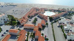 An aerial view of a coastal hotel with multiple buildings, a central swimming pool, and a beach in the background.