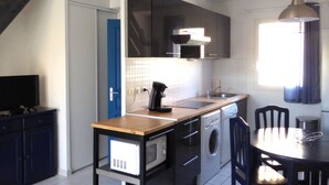 A compact kitchen with a washing machine, a coffee maker, and a dining area with a table and chairs.