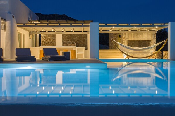 Un espace piscine extérieur moderne, doté de chaises longues, d’un hamac et d’une cheminée en pierre.