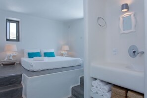 Une chambre à coucher comprenant un lit, deux tables de chevet avec des lampes, une fenêtre et une salle de bain avec une baignoire et des serviettes.