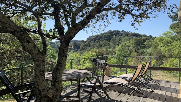 Une terrasse en bois avec une table et des chaises, offrant une vue sur une colline boisée.