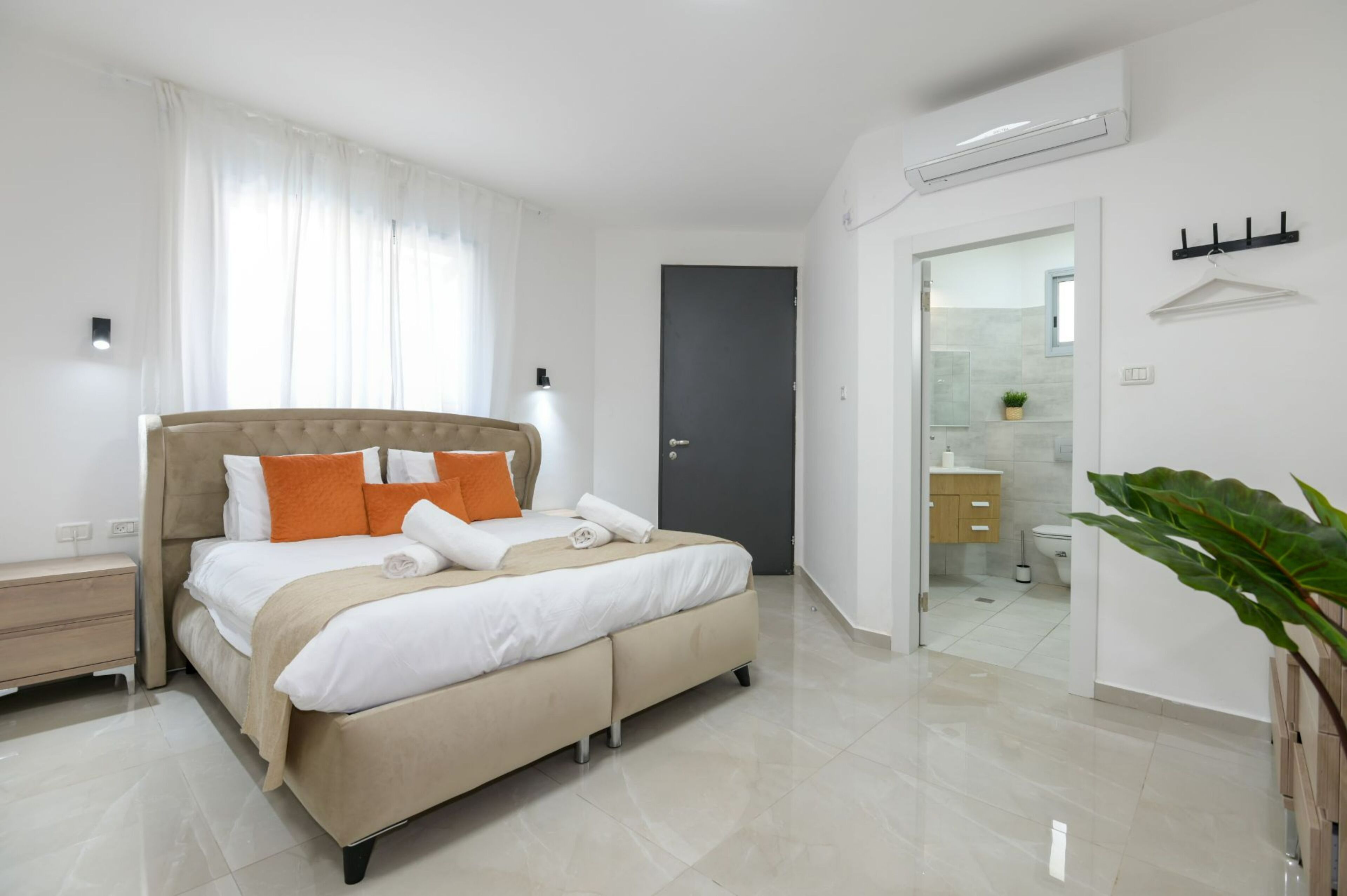 Un dormitorio moderno con una cama grande, una mesita de noche, un armario y un baño visible a través de una puerta abierta.