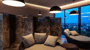Une chambre moderne avec un grand lit, deux fauteuils et une vue sur la ville au crépuscule.