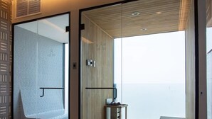 Une chambre d’hôtel moderne dotée d’une porte vitrée donnant sur un balcon, d’une petite table avec une chaise et d’un plancher en bois.