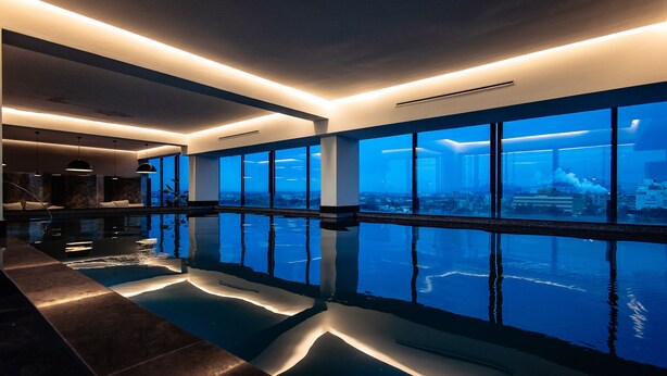 Un espace piscine intérieur moderne, doté de grandes fenêtres offrant une vue sur le paysage urbain.