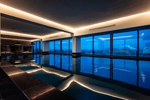 Un espace piscine intérieur moderne, doté de grandes fenêtres offrant une vue sur le paysage urbain.