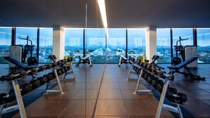 Une salle de sport équipée de matériel d’exercice et dotée de grandes fenêtres offrant une vue sur la ville.