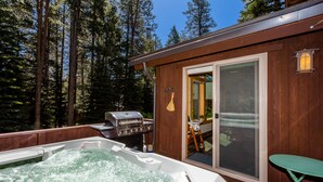 A hot tub with a wooden deck, a grill, and a sliding glass door leading to a deck area. - Prosser Paradise_Hot Tub, Arcade, Walk 2 Prosser Reservoir, Exercise Equip, Kid Toys & Air Purifiers (Truckee)