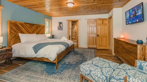 A bedroom with a wooden ceiling, a bed with a blue and white patterned bedspread, a wooden dresser, and a television on the wall. - Prosser Paradise_Hot Tub, Arcade, Walk 2 Prosser Reservoir, Exercise Equip, Kid Toys & Air Purifiers (Truckee)