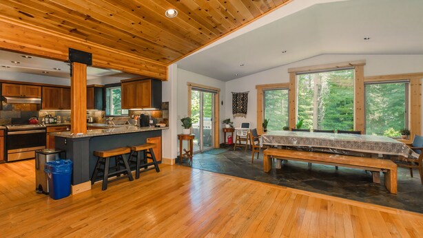 A spacious kitchen with wooden flooring, a central island with stools, and large windows offering a view of the outdoors. - Prosser Paradise_Hot Tub, Arcade, Walk 2 Prosser Reservoir, Exercise Equip, Kid Toys & Air Purifiers (Truckee)