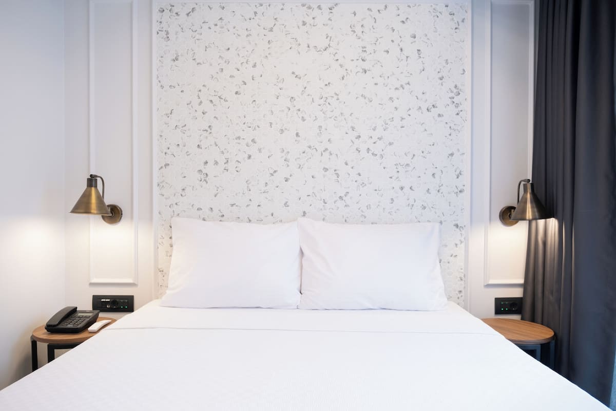 A neatly made bed with white linens, two bedside lamps, a bedside phone, and a small table with a lamp.