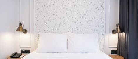 Una cama bien hecha con ropa blanca, dos lámparas de noche, un teléfono en la mesita y una pequeña mesa con lámpara.
