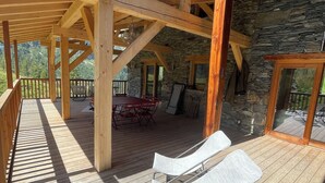 A wooden deck with a stone wall, a covered seating area, and a view of the outdoors. - Chalet au Sud, Face aux Glaciers (Tignes)