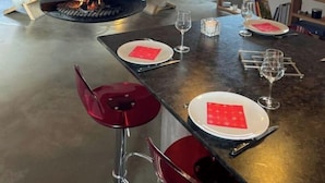 A modern kitchen with a central wood-burning stove, a dining area with a round table set for four, and a cozy living space in the background. - Chalet au Sud, Face aux Glaciers (Tignes)