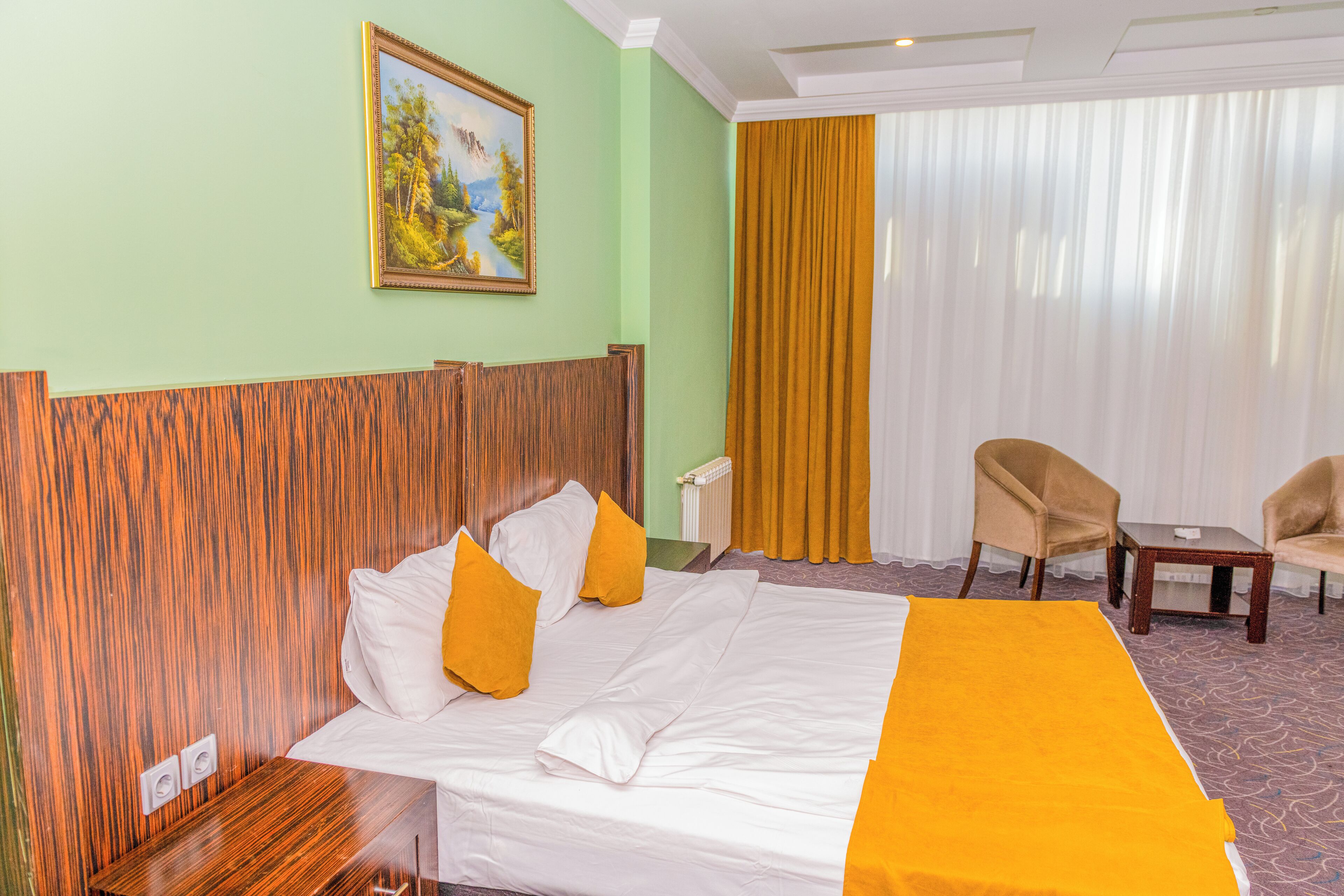 A hotel room with a large bed, two chairs, a small table, and a painting on the wall.