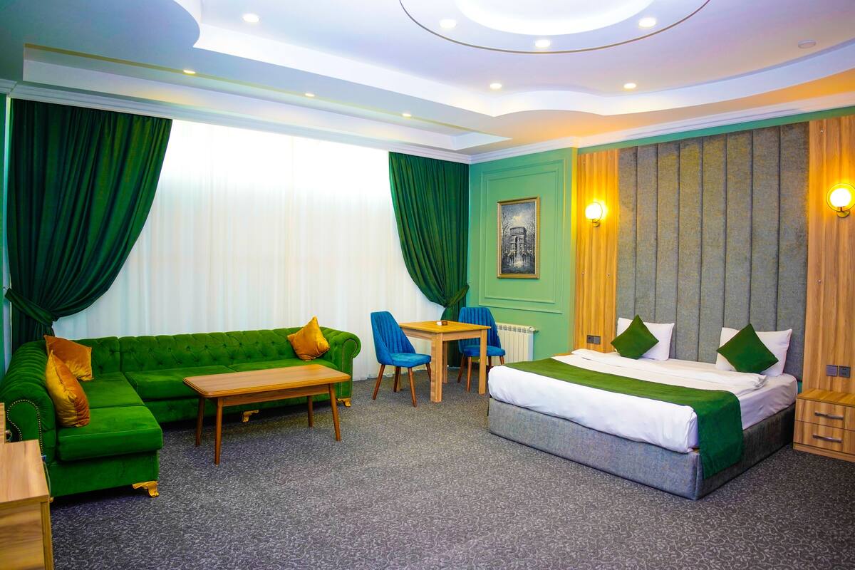 Une chambre d’hôtel avec un canapé vert, un lit, une table en bois et deux chaises.