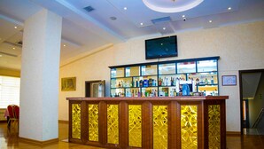 Una hall d'hotel con una reception, un televisore a parete e una scala sullo sfondo.