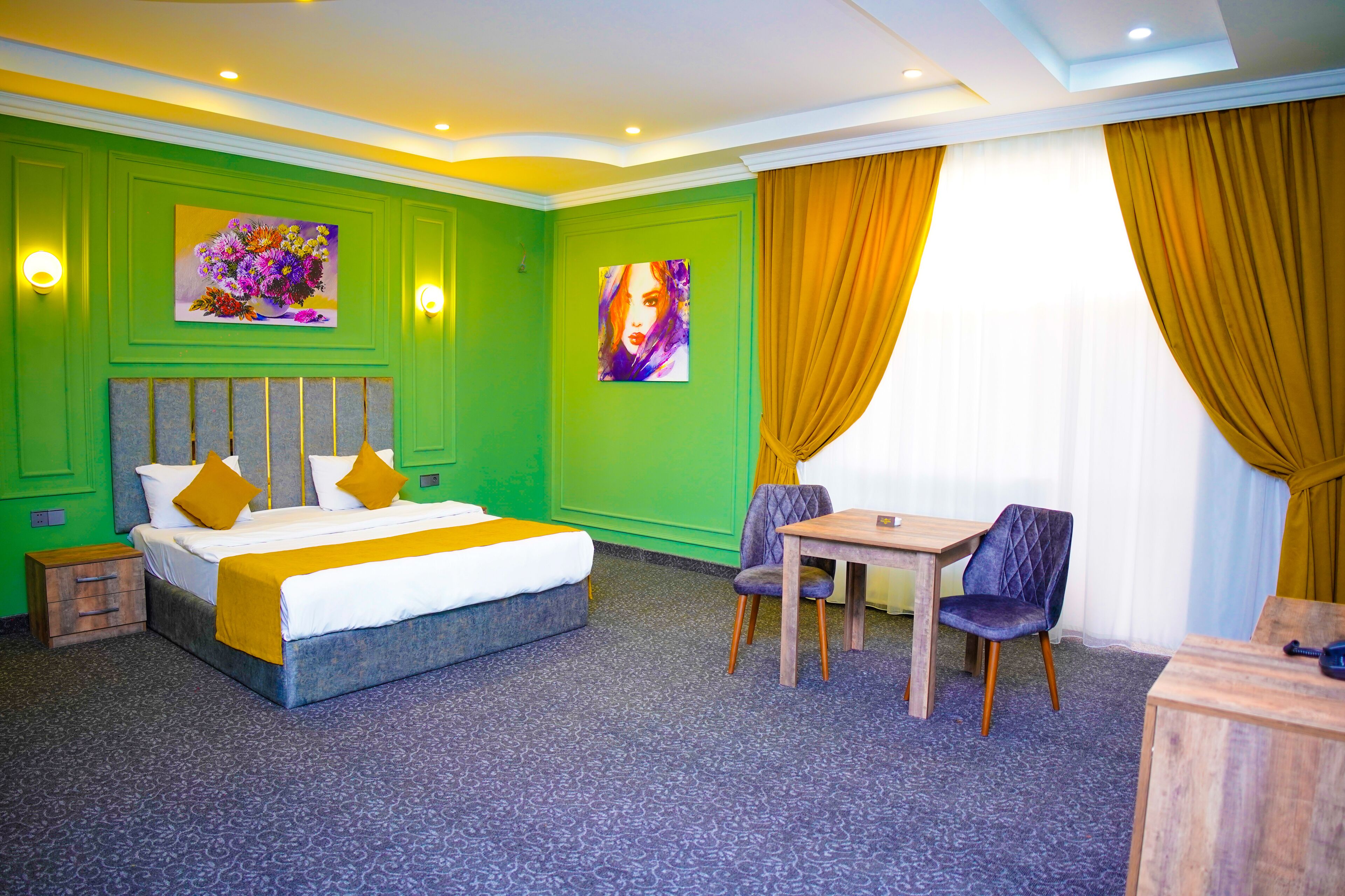 A hotel room with a bed, two chairs, a small table, and artwork on the walls.