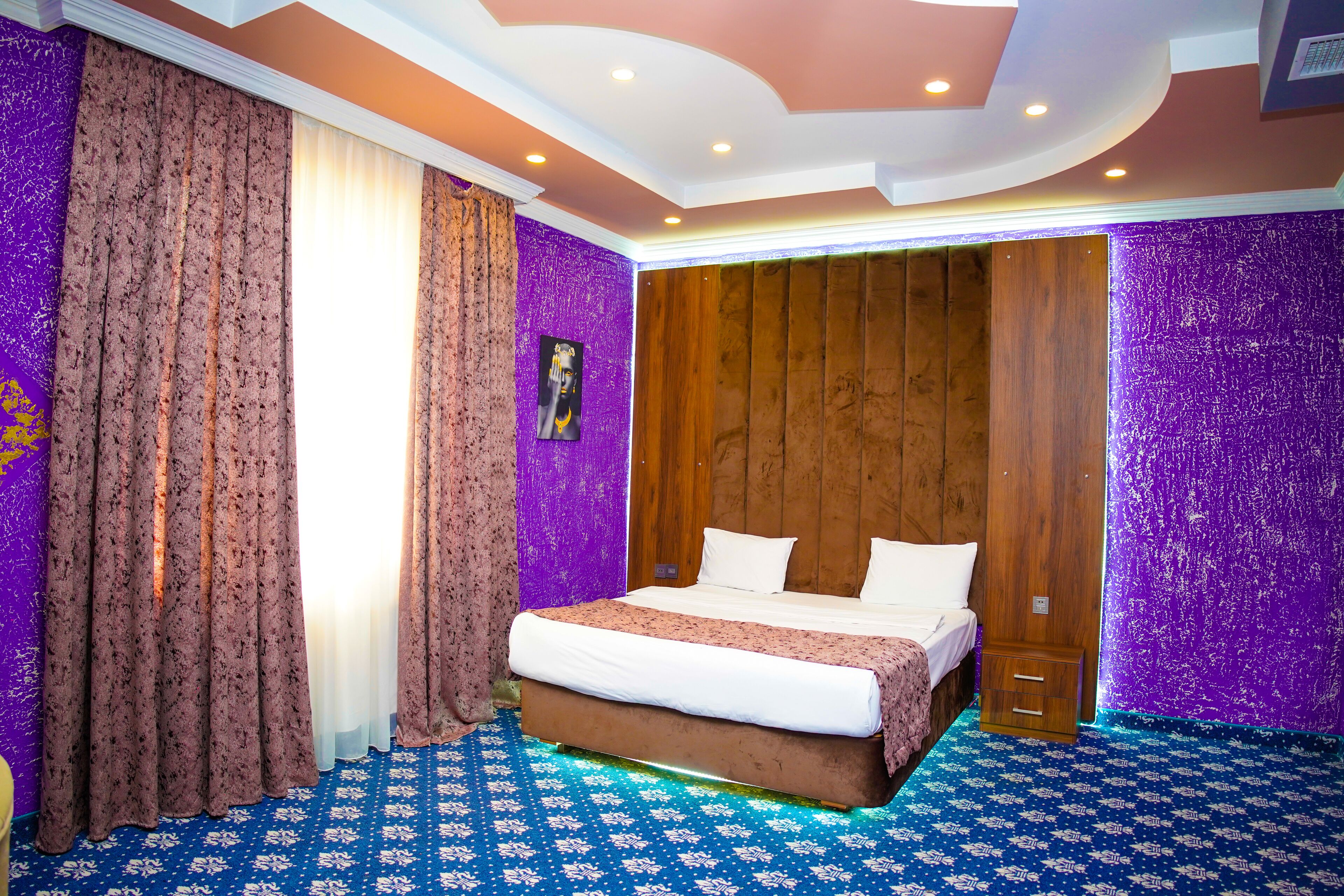 Une pièce avec un lit, des rideaux, un mur recouvert de panneaux en bois et une moquette à motifs.