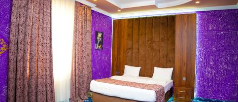 Une pièce avec un lit, des rideaux, un mur recouvert de panneaux en bois et une moquette à motifs.
