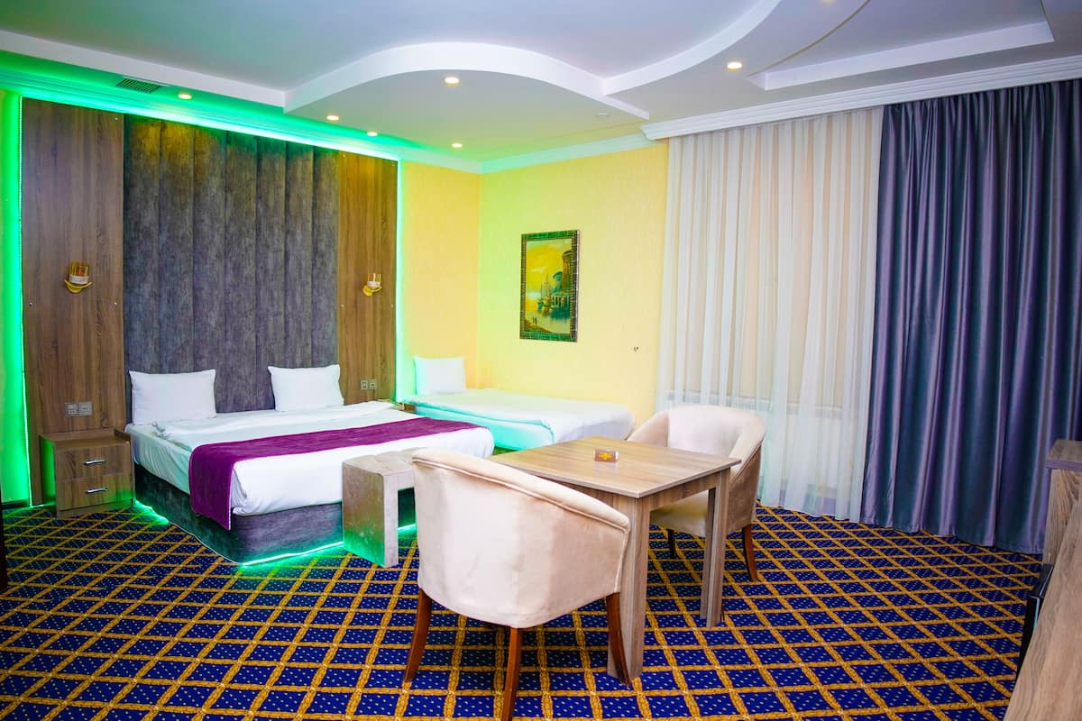 Une chambre d’hôtel comprenant un lit, deux tables de chevet, une chaise, une petite table, une commode et une fenêtre avec des rideaux.