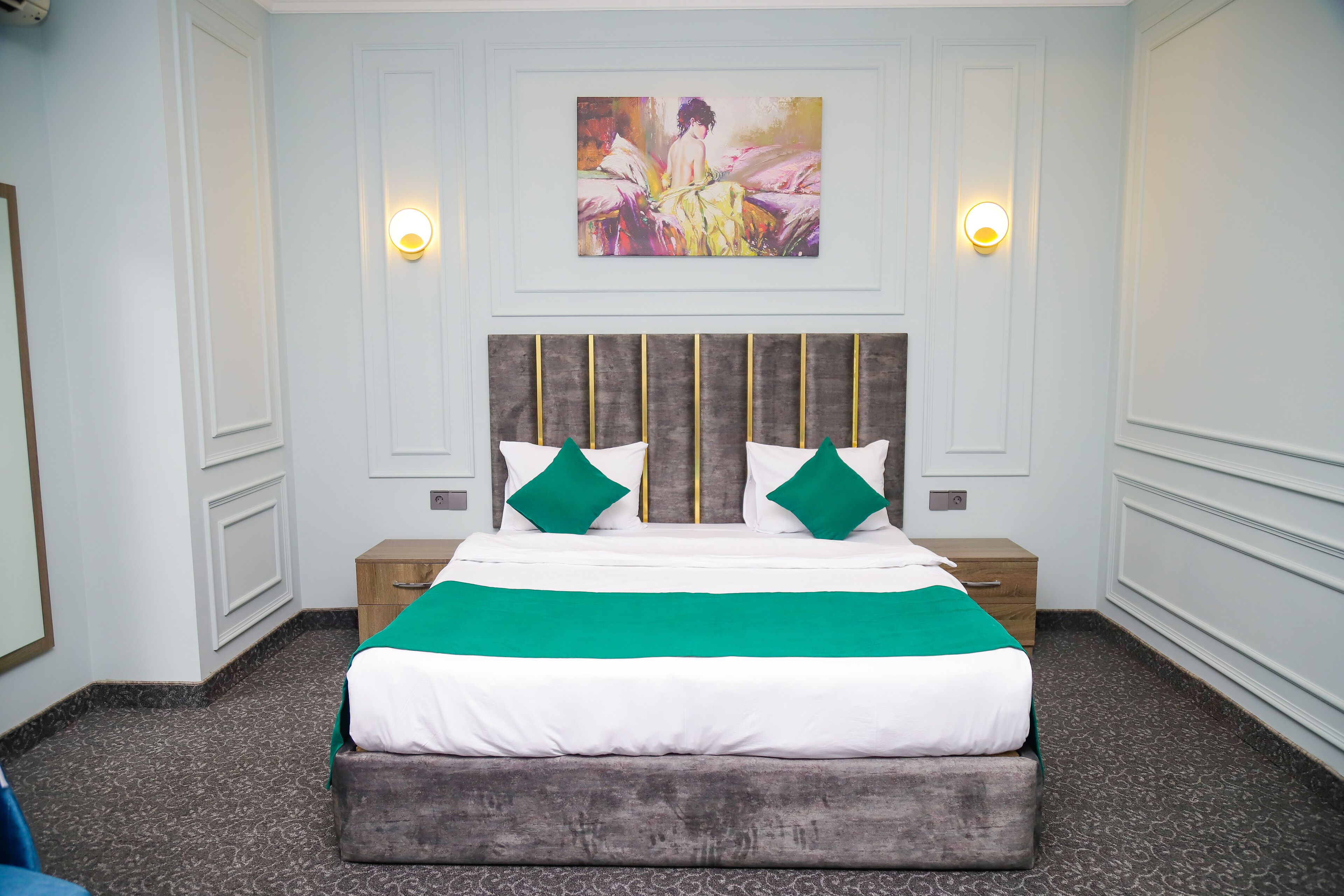 A neatly arranged bedroom with a large bed, two nightstands, a headboard with vertical slats, and a painting above the bed.