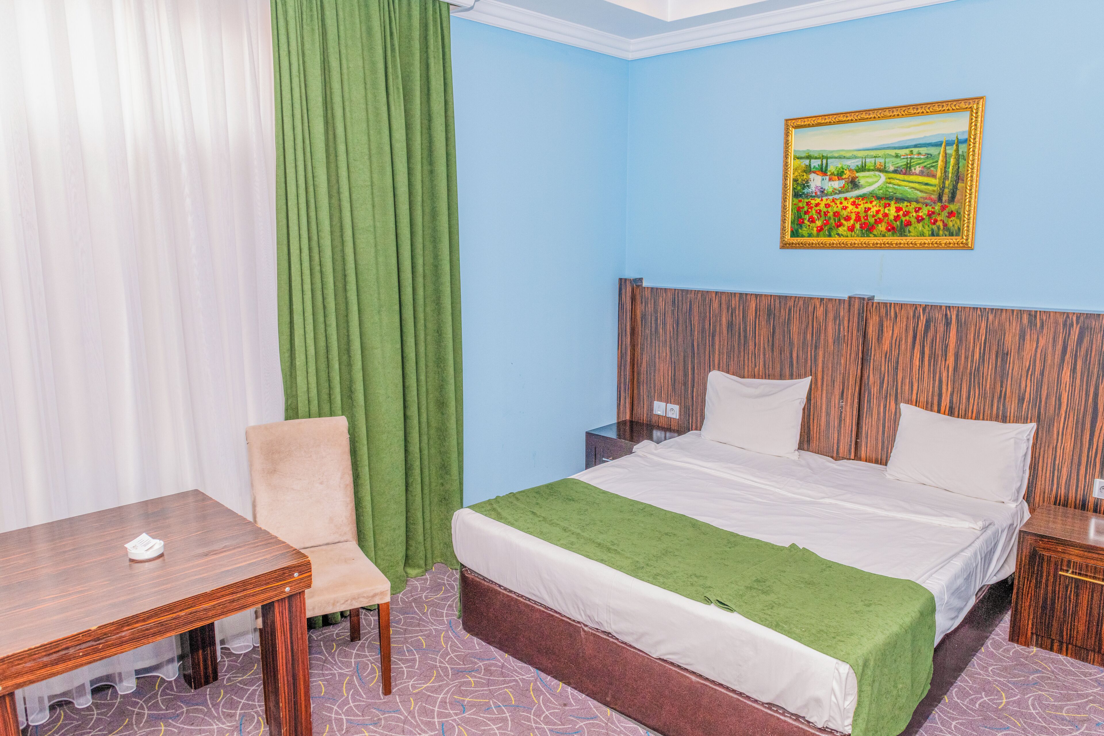 A hotel room with a bed, a chair, a table, and a painting on the wall.