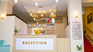 Un'area reception con un cartello 'RECEPTION', orologi, bandiere e una bacheca a parete.
