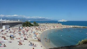 En fullsatt strand med folk som solar och badar, en klar himmel och en båt i fjärran.