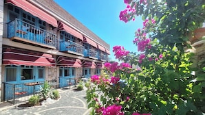 Een hotel met meerdere balkons, buitenmeubels en levendige bougainvillea bloemen.