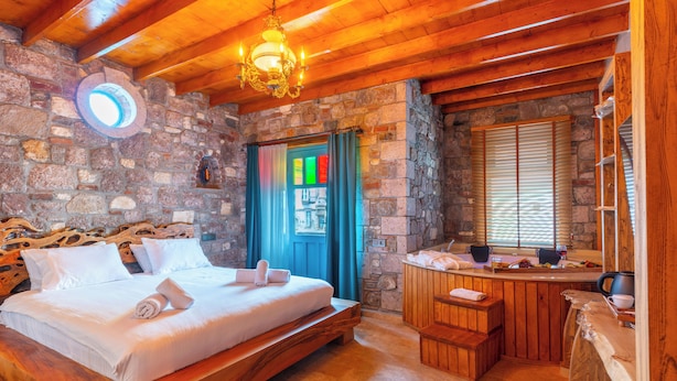 Een slaapkamer met houten frame, een stenen muur, een bed, een klein houten bankje en een stenen open haard.