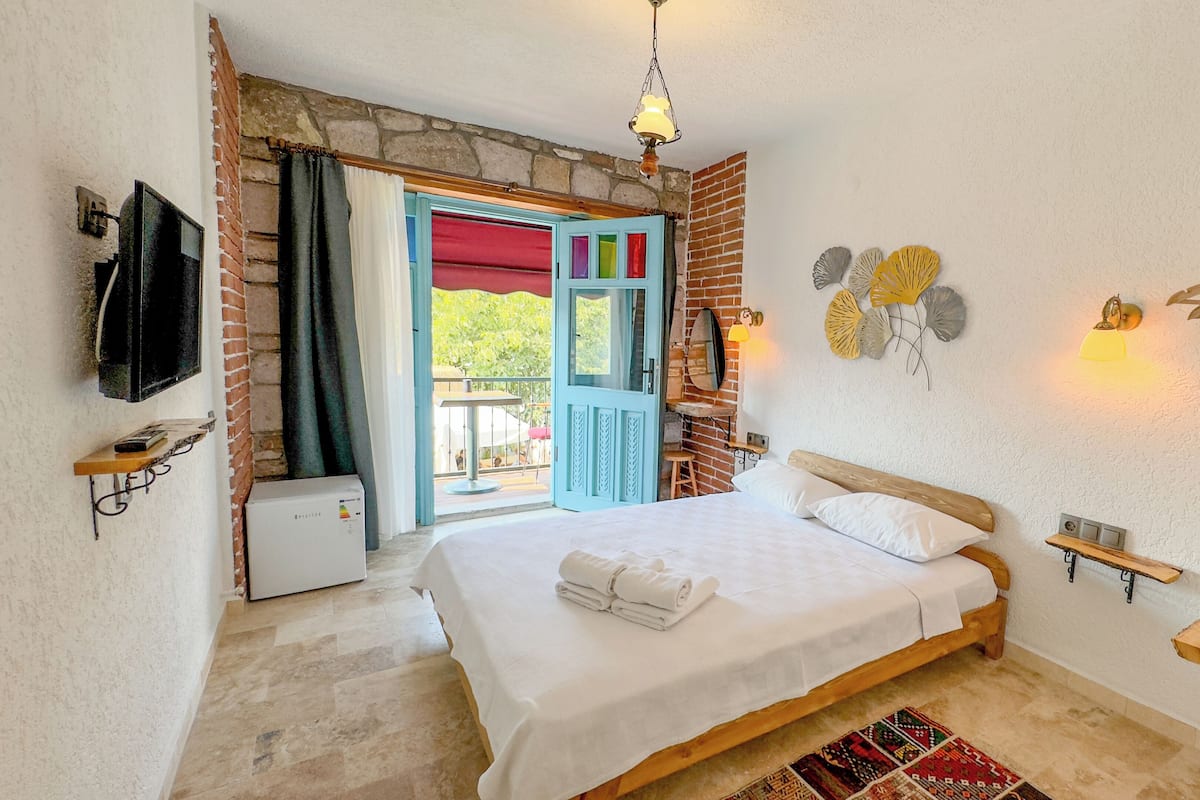 Un dormitorio con cama, televisión, calefacción, ventana con cortinas y balcón.