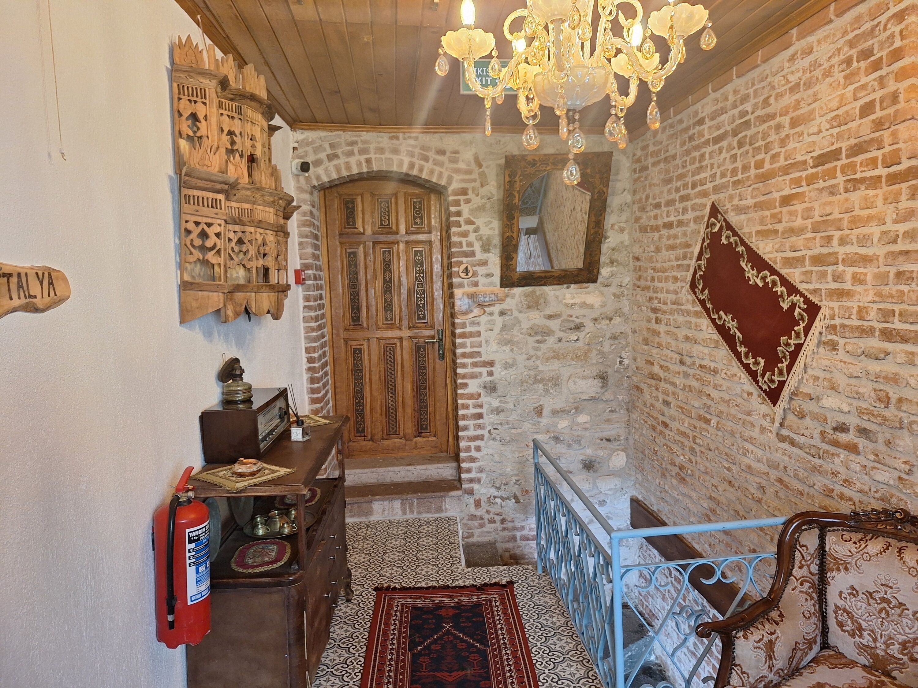 A hallway with a wooden door, a fire extinguisher, a chandelier, and a patterned rug.