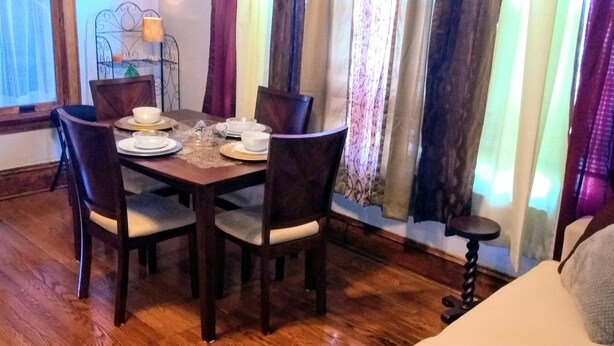 Un comedor con una mesa de madera, cuatro sillas y una mesita auxiliar con una lámpara.