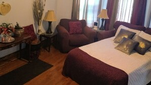 Un dormitorio bien iluminado con una cama grande, dos sillones, una mesita y un ventilador de techo.