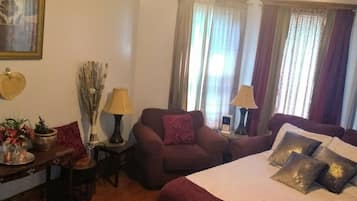 A well-lit bedroom with a large bed, two armchairs, a small table, and a ceiling fan.