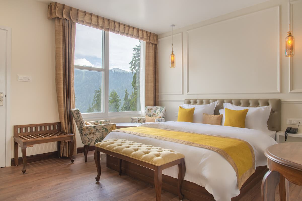 Ein Schlafzimmer mit einem großen Bett, einer Bank, einem Stuhl und Bergblick durch ein Fenster.