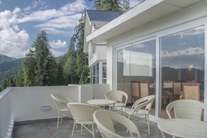 Un edificio moderno con balcón de vidrio, muebles de mimbre y vistas a las montañas.