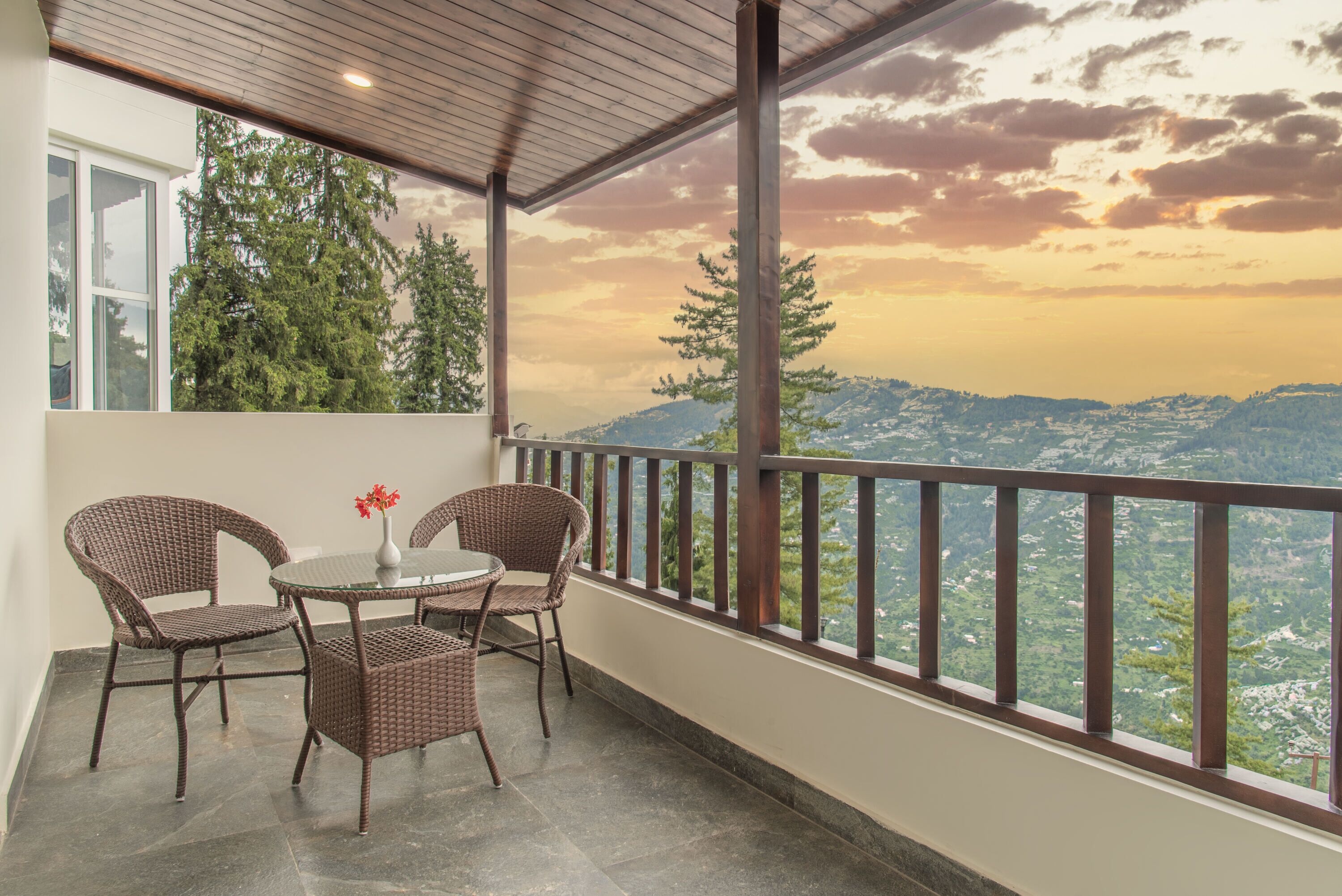 A balcony with wicker chairs and a table, overlooking a mountainous landscape.