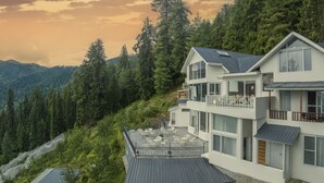 A two-story building with a balcony, surrounded by dense forest and mountains. - Echor Backwoods Villa Narkanda (Kumharsain)