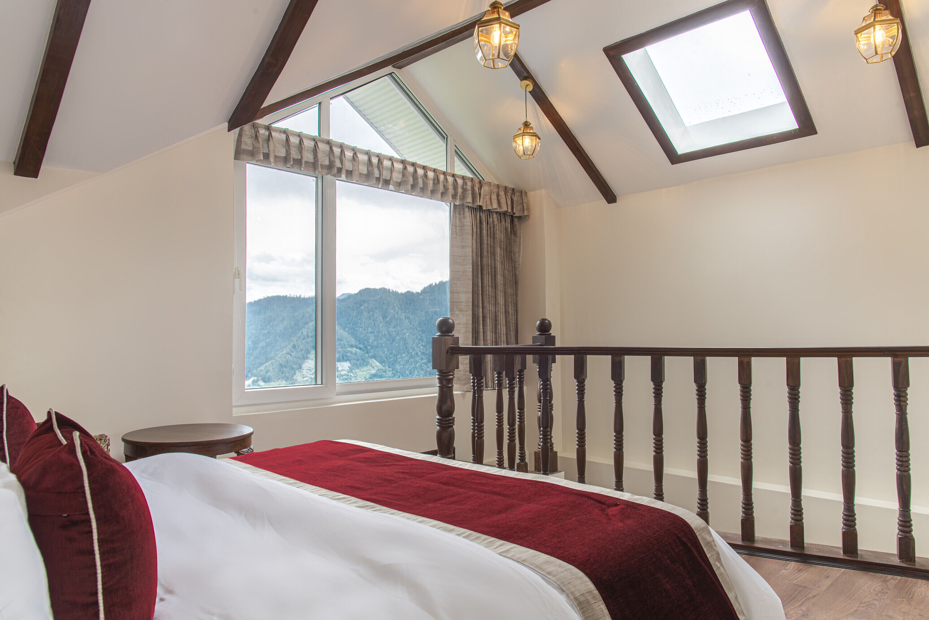 Un dormitorio con una ventana grande, una cama de madera con ropa de cama roja y vistas a las montañas.