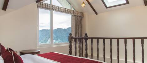 Un dormitorio con una ventana grande, una cama de madera con ropa de cama roja y vistas a las montañas.