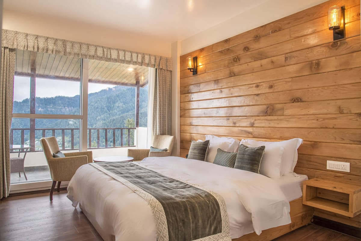 Ein Schlafzimmer mit einem großen Bett, Holzpaneelen an der Wand, Blick ins Freie und einem Sessel am Fenster.