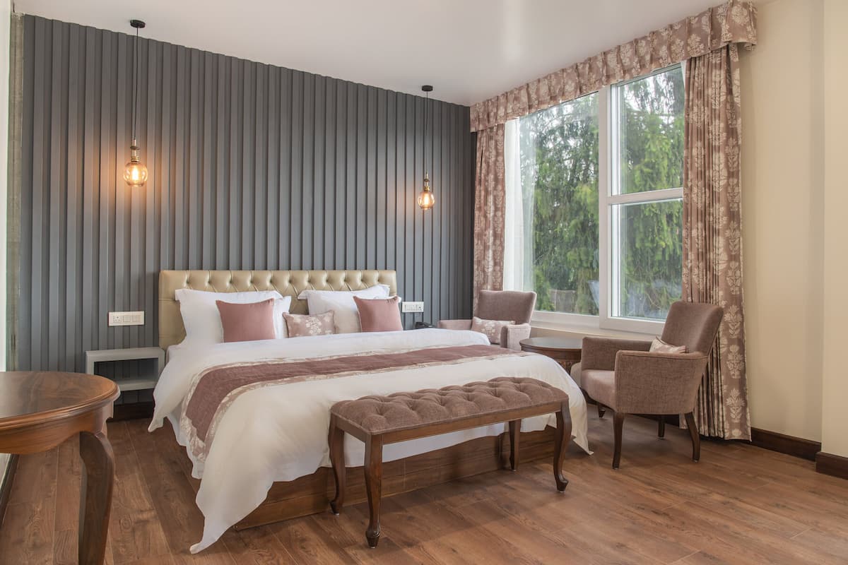 Ein Schlafzimmer mit einem großen Bett, einer Bank, zwei Stühlen, einem Nachttisch und einem fenster mit Vorhängen.