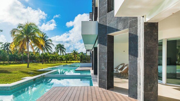 A modern pool area with a wooden deck, a clear pool, and palm trees in the background. - NEW 2BR Swim-Up at Mareazul Resort – Sleeps 6 | Casa Bellissima (Playa del Carmen)