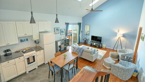 Een moderne keuken met witte kasten, een eetgedeelte met een houten tafel en stoelen, en een woonkamer met een bank en gestreept fauteuils.