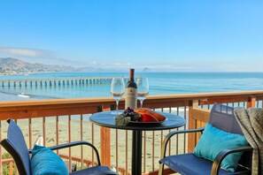 A table with a bottle of wine, two glasses, and a plate of fruit on a balcony overlooking the ocean. - Charming Seaside Retreat by Cayucos Pier (Cayucos)