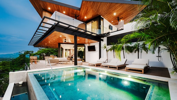 Una casa moderna con piscina, terraza de madera y sillones de descanso.