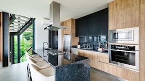 Una cocina moderna con una isla central, electrodomésticos de acero inoxidable y vistas a zonas verdes a través de amplias ventanas.