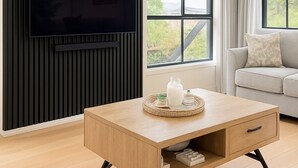 Een moderne woonkamer met een houten salontafel, een wandgemonteerde televisie en een groot raam met gordijnen.